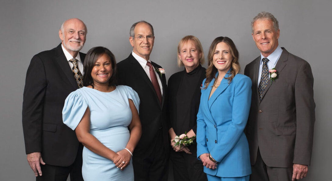 A group of people posing in front of a grey backgound.